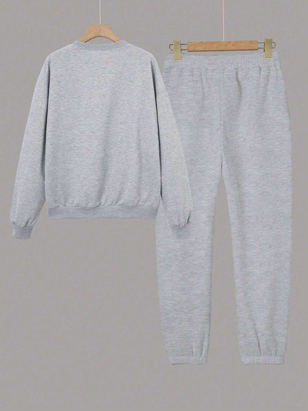 Gray sweatshirt and pants set on hangers against a gray background