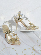 Gold high-heeled sandals with leaf designs on a white background