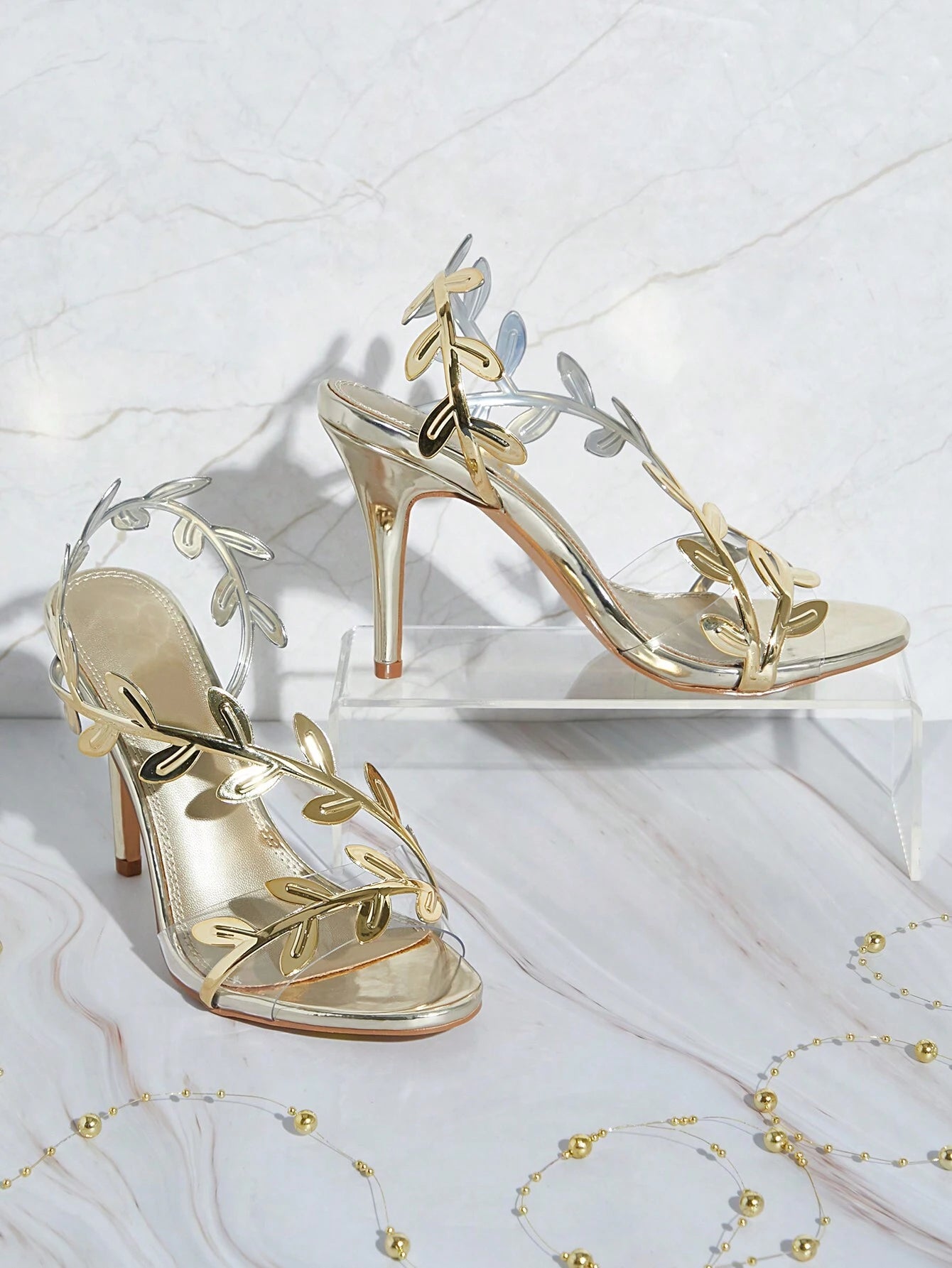 Gold high-heeled sandals with leaf designs on a white background