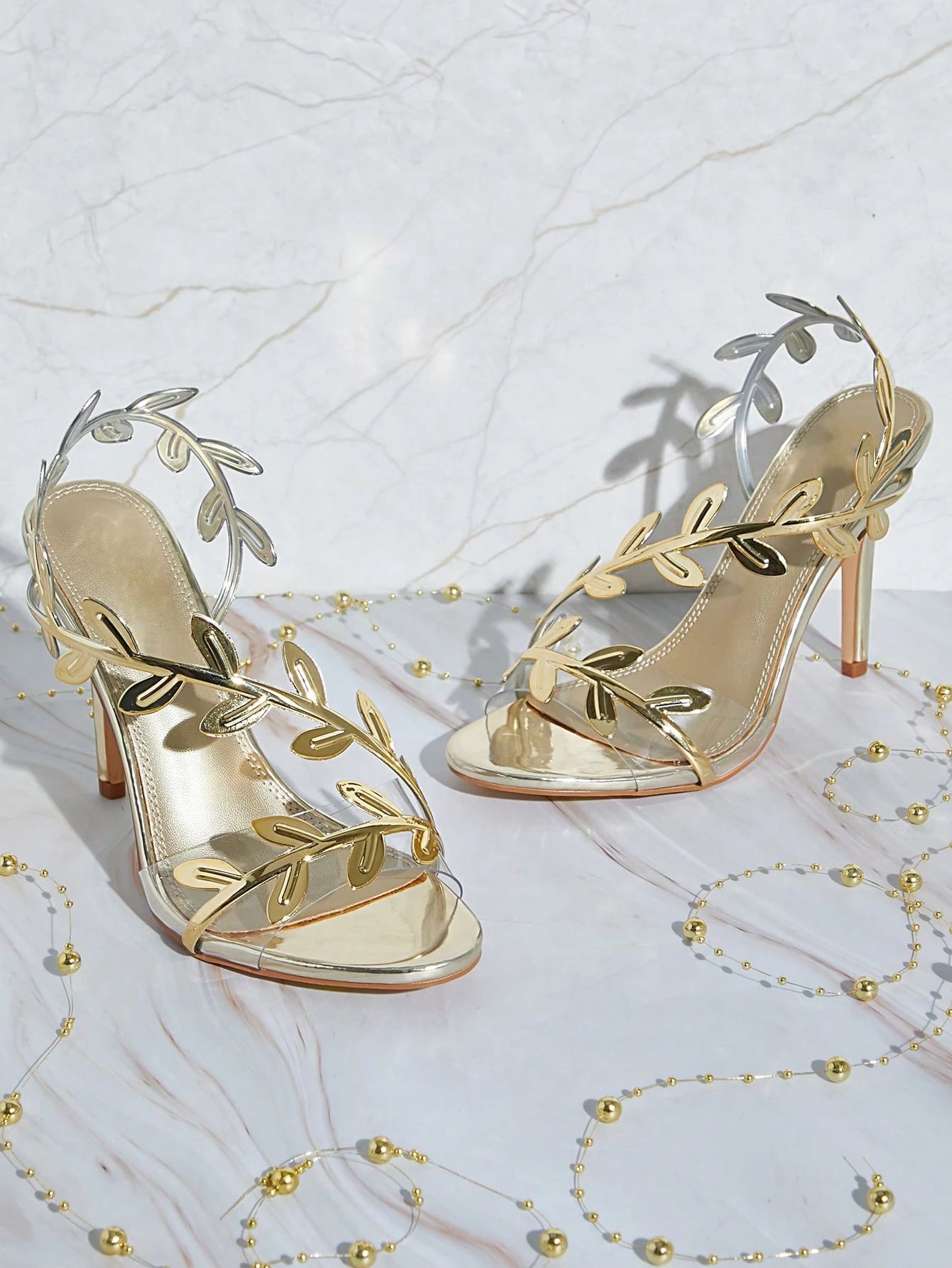Gold high-heeled sandals with leaf designs on a white background