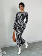 Woman wearing a patterned dress with white shoes and a brown bag against a plain background