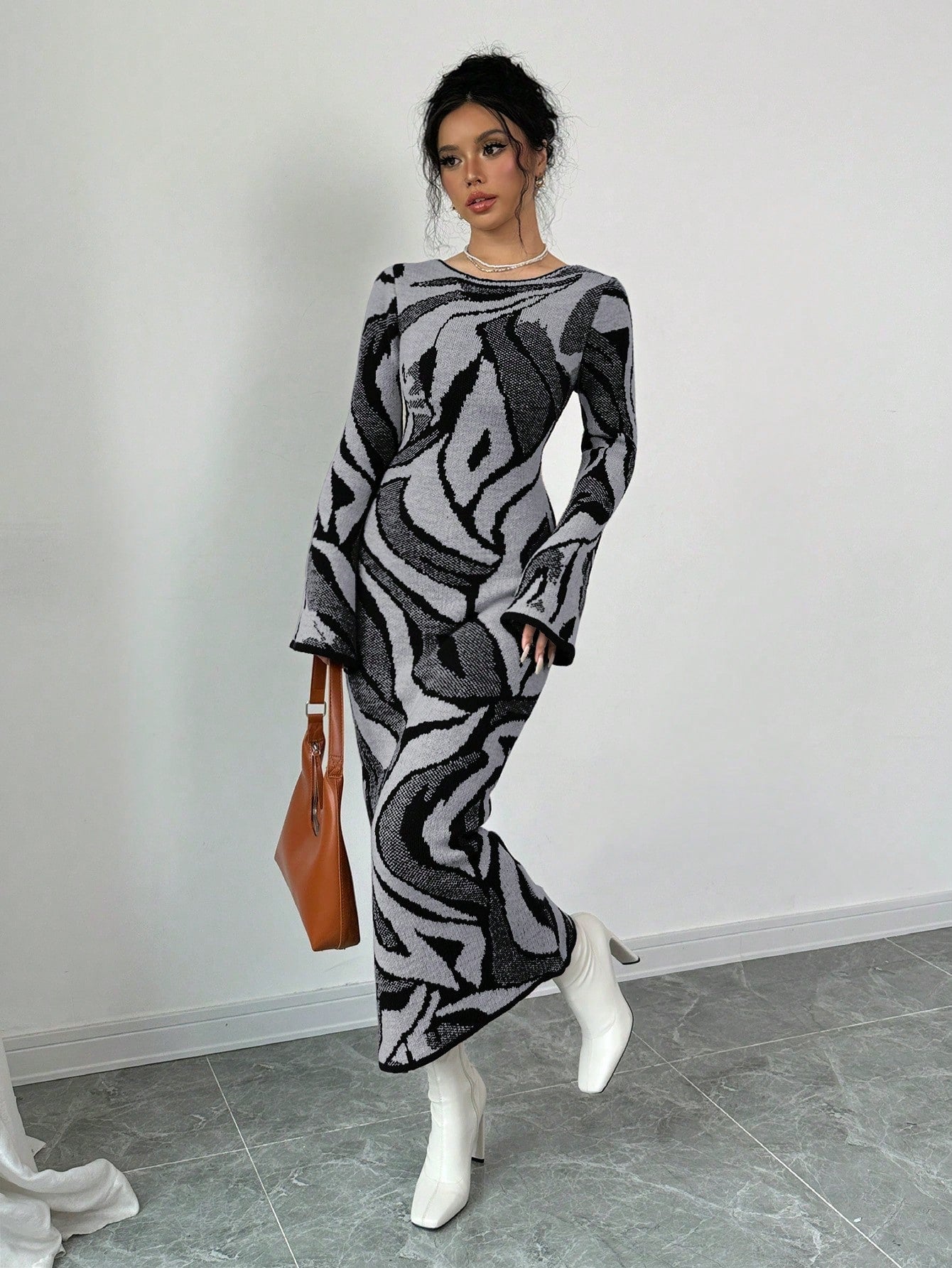 Woman wearing a patterned dress with white shoes and a brown bag against a plain background