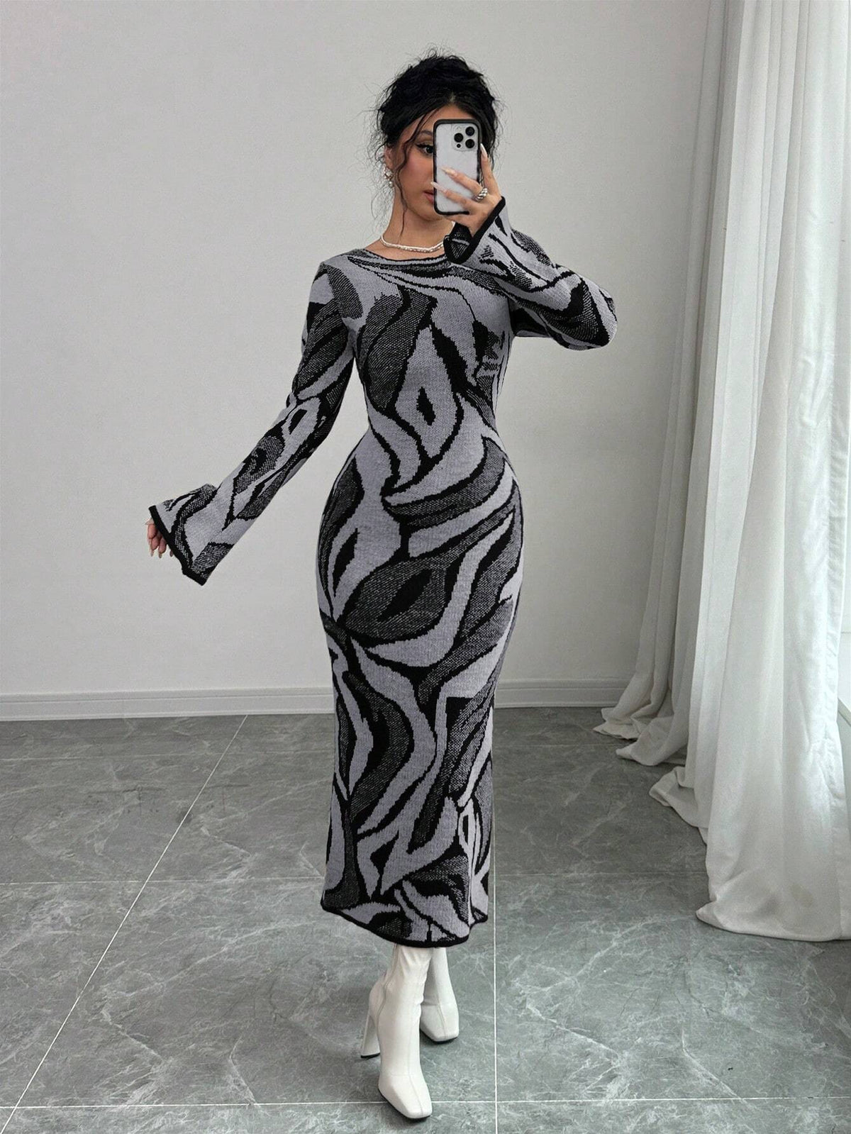 Person wearing a patterned dress in a room with a white curtain and gray floor.