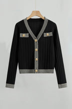 Black cardigan with silver trim and gold buttons on a hanger against a light gray background
