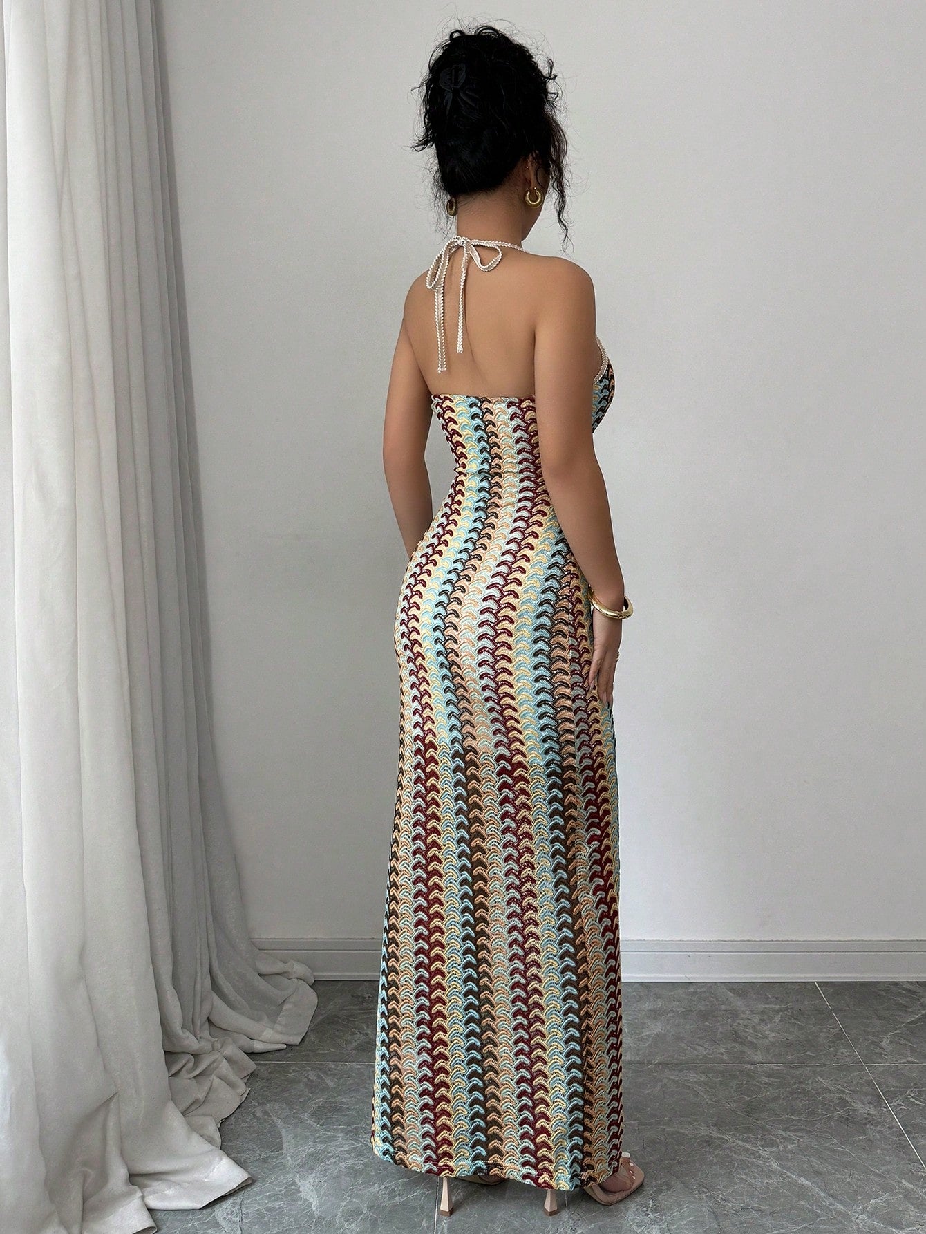 Woman wearing a long, patterned dress standing in a room with white curtains.
