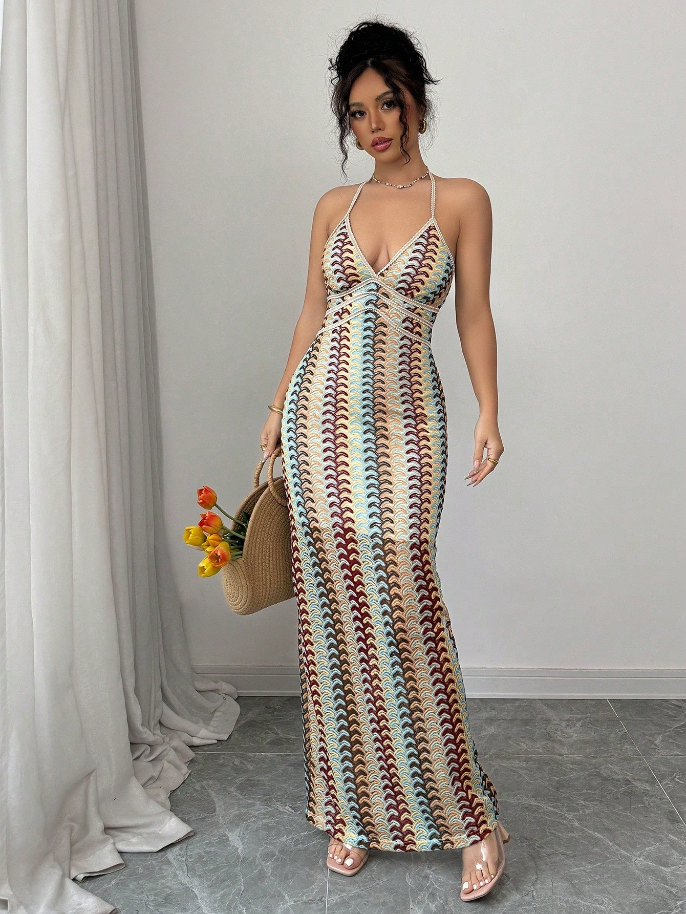 Woman wearing a colorful patterned dress holding a woven handbag indoors.