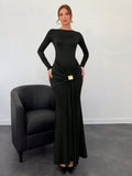 Woman wearing a black evening gown standing next to a black chair against a white wall.