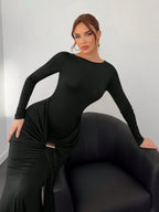 Woman wearing a black long-sleeve dress sitting on a black chair against a light gray background