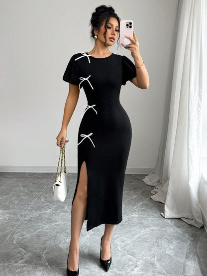 Woman in a black dress with white accents taking a mirror selfie.
