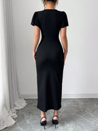 Person wearing a black dress standing in a room with white walls and gray floor.