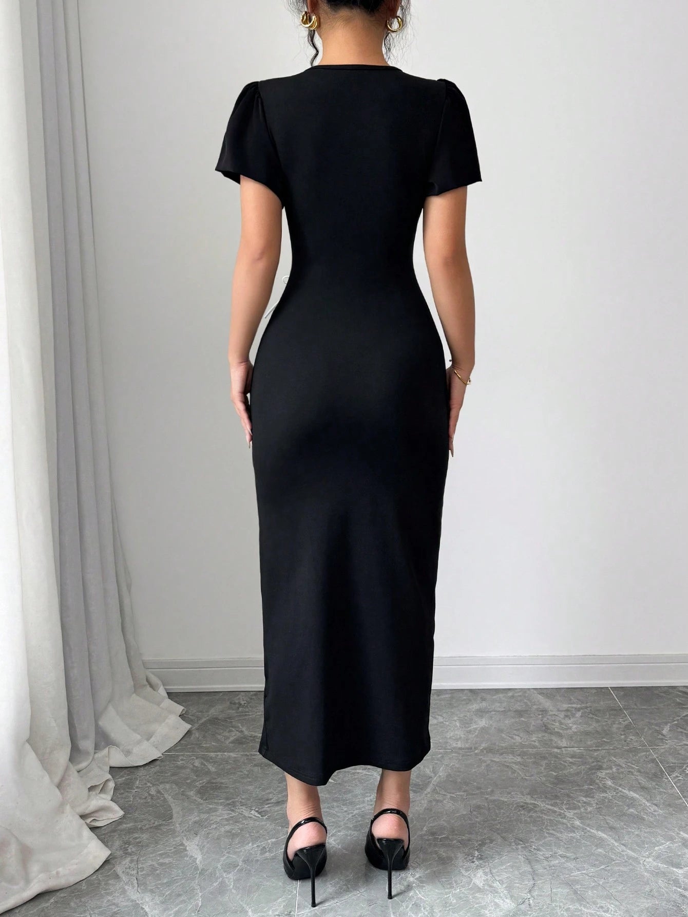 Person wearing a black dress standing in a room with white walls and gray floor.