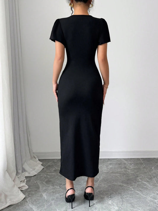 Person wearing a black dress standing in a room with white walls and gray floor.