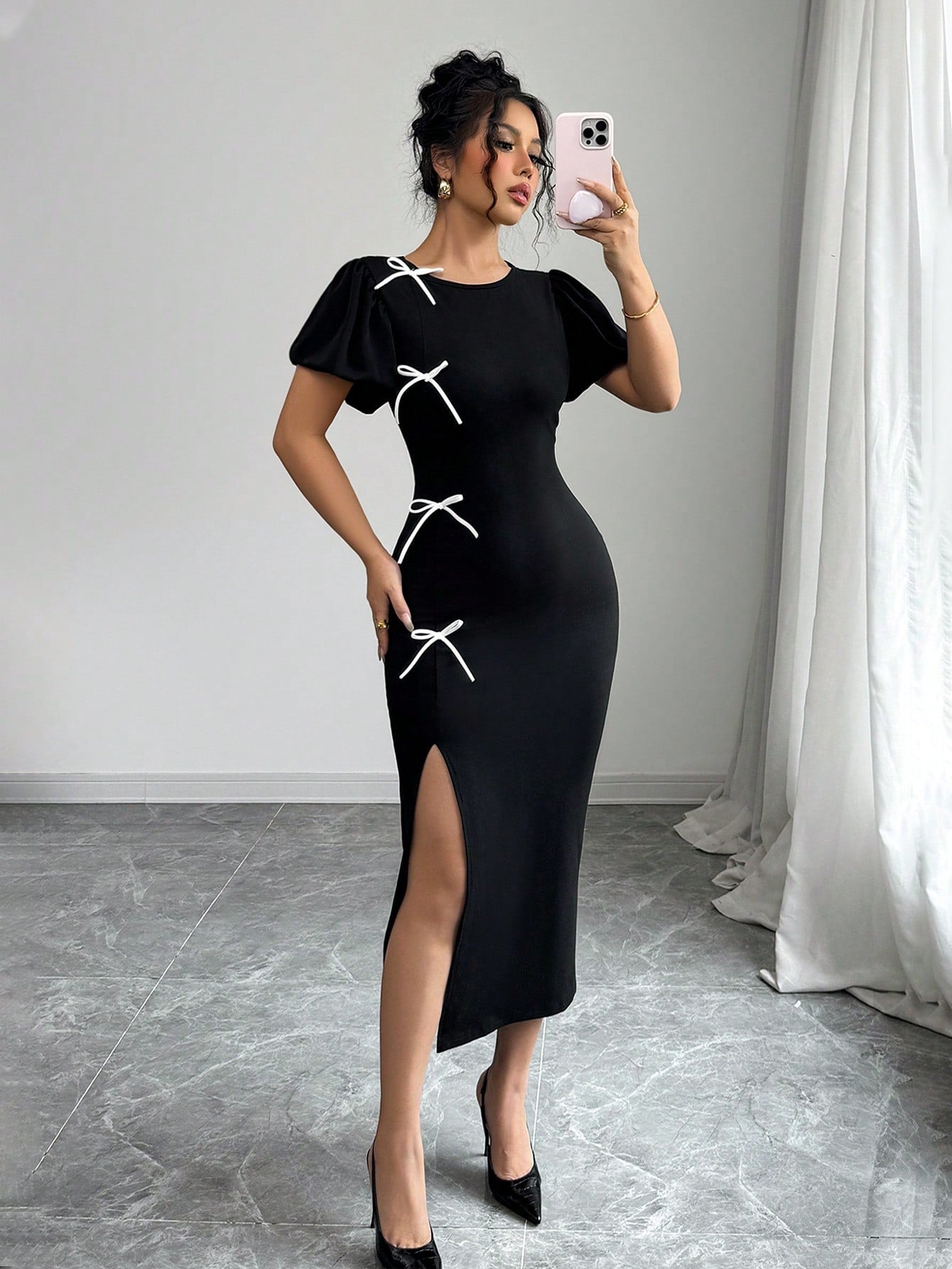 Woman wearing a black dress with white bow details, standing indoors.
