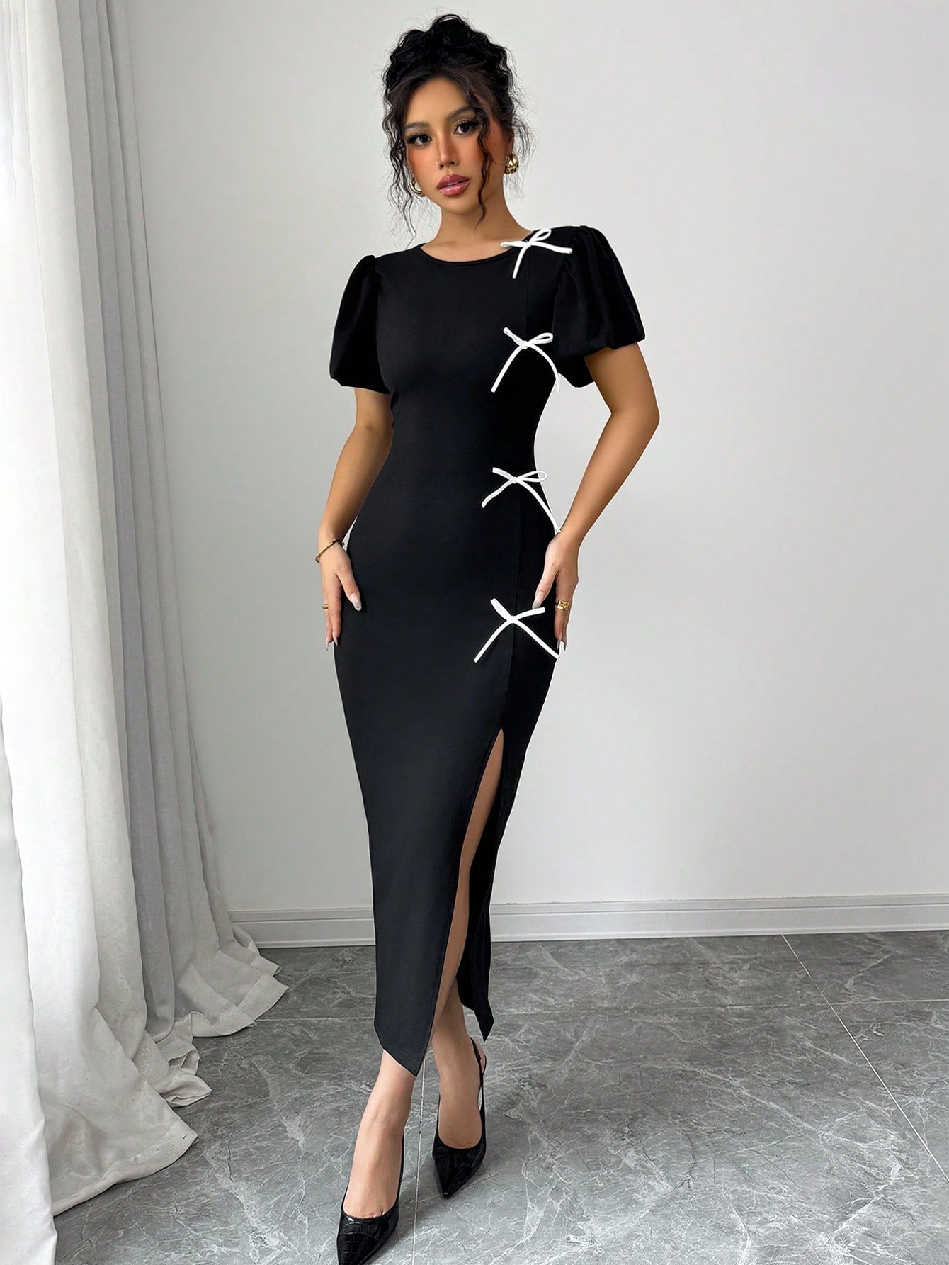 Woman wearing a black dress with white lace details against a white wall.