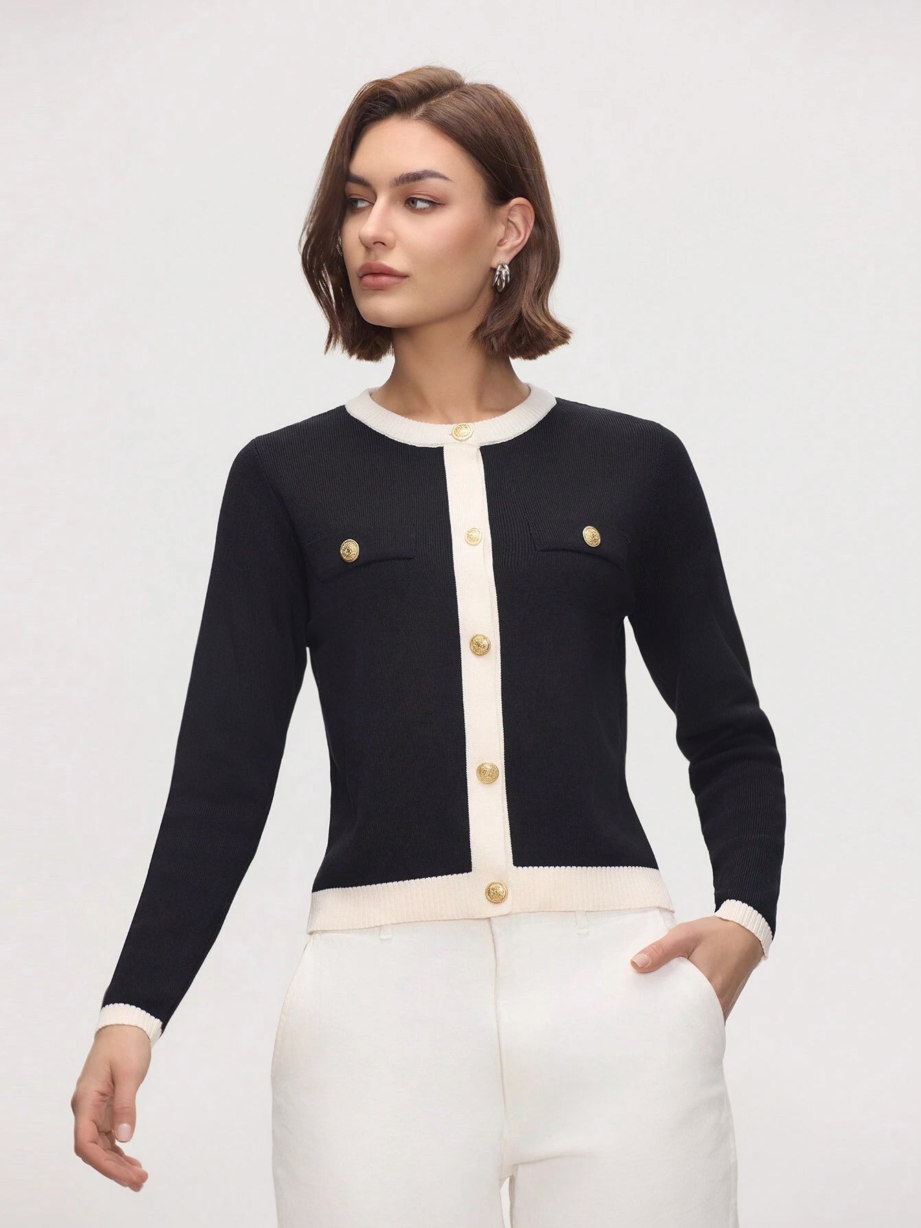 Woman wearing a black and white cardigan with gold buttons on a plain background
