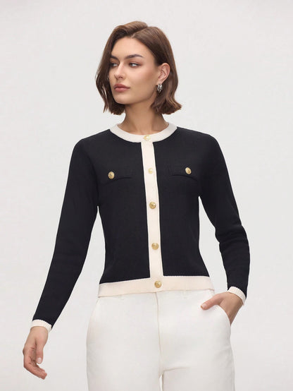 Woman wearing a black and white cardigan with gold buttons on a plain background