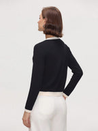 Woman wearing a black long-sleeve top with a white collar against a light gray background