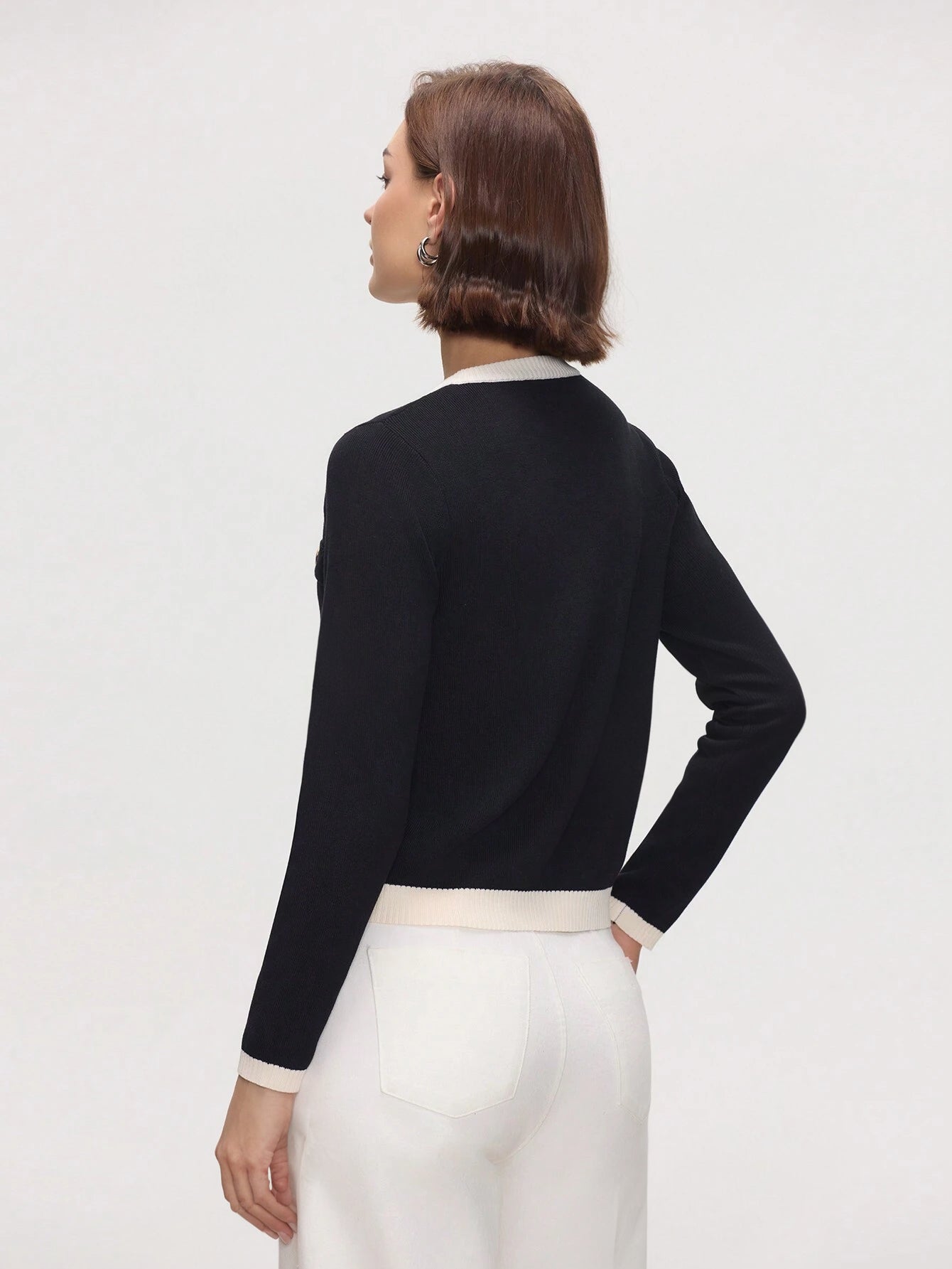 Woman wearing a black long-sleeve top with a white collar against a light gray background
