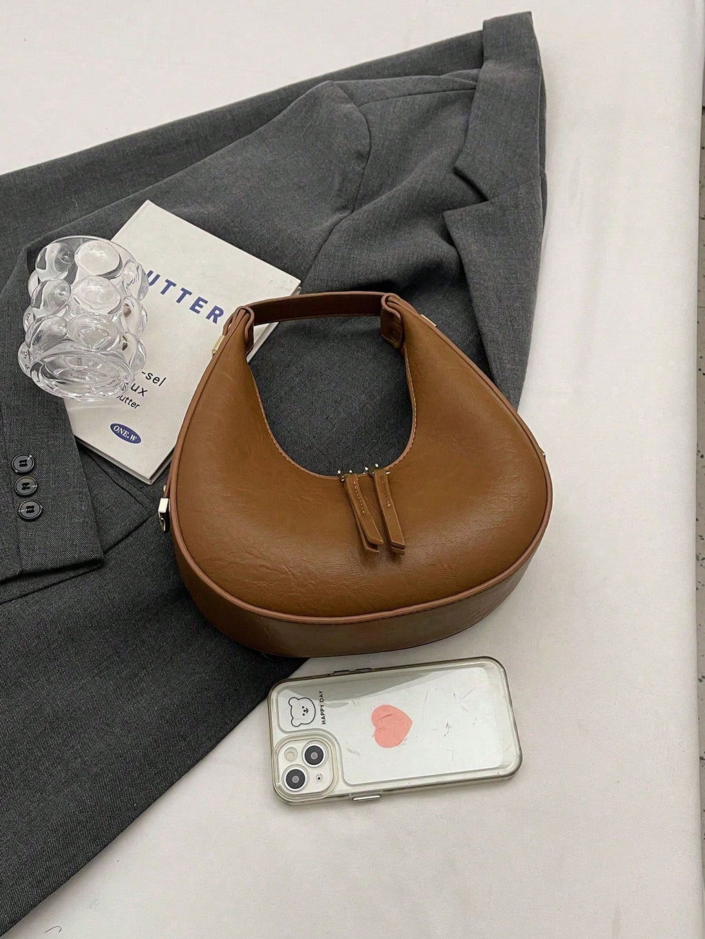 Brown leather handbag on a gray suit with a phone and glass of water