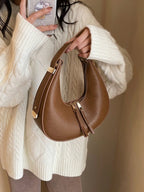 Brown handbag held by a person wearing a white sweater against a neutral background