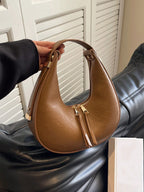 Brown handbag held by a person against a neutral background