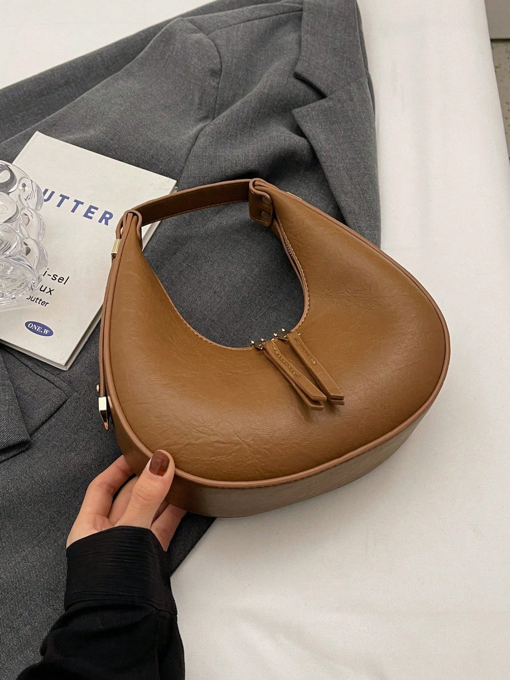 Brown handbag held by a hand on a gray fabric background