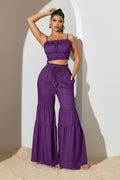 Woman wearing a purple outfit with a top and tiered pants against a neutral background