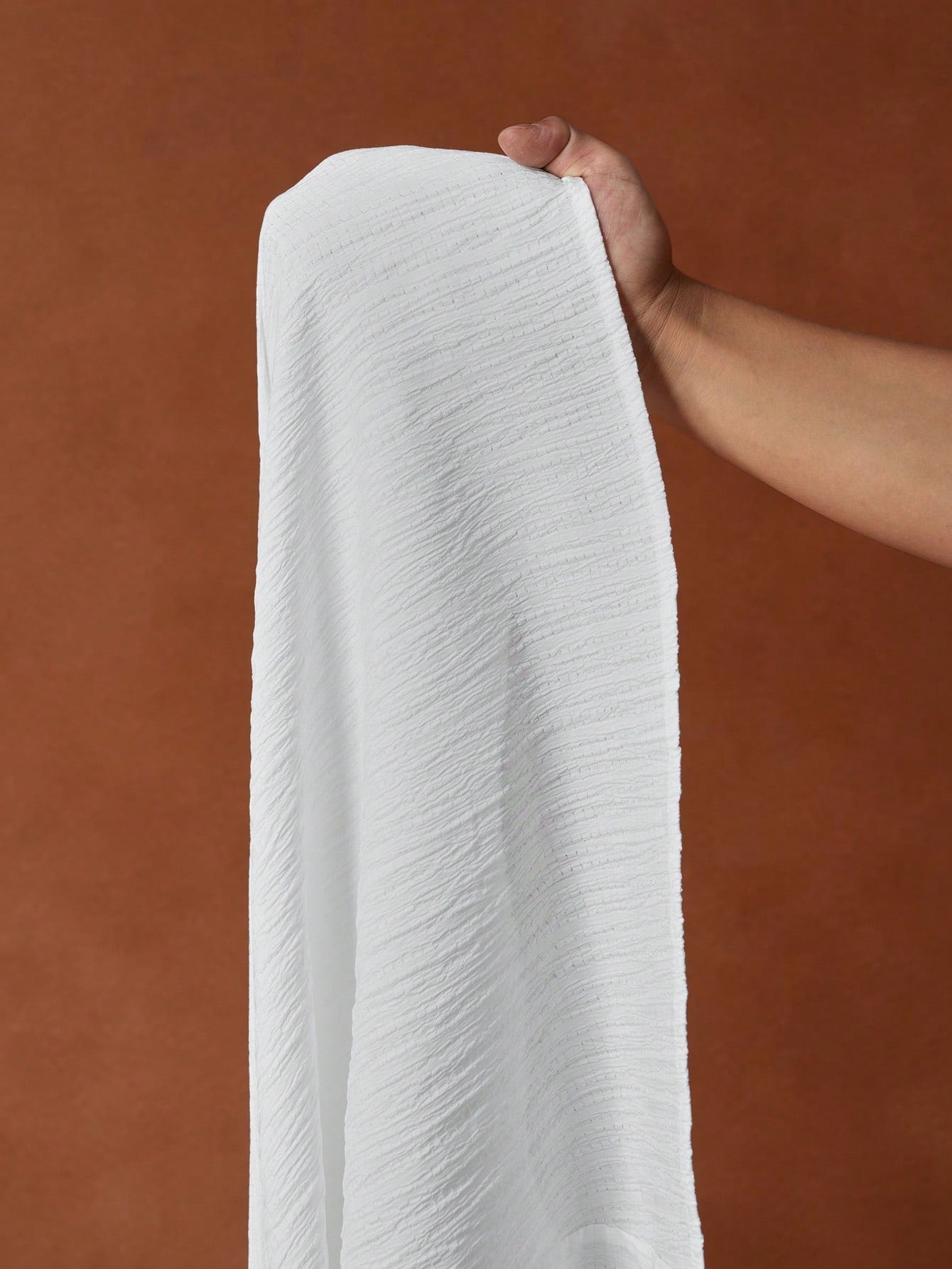 Hand holding a roll of white paper towels against a brown background