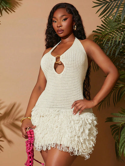 Woman wearing a white crochet dress with ruffled hem against a beige background with green foliage.