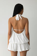 White halter neck dress with a tie at the back on a plain background