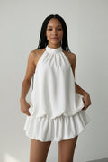 Woman wearing a white halter top and shorts against a plain background