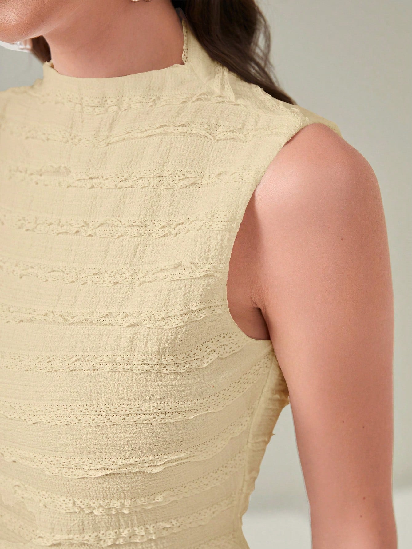 Close-up of a person wearing a beige textured sleeveless top against a neutral background