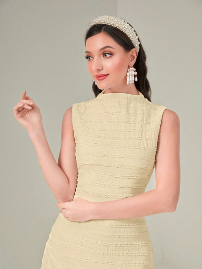 Woman wearing a light green dress with a textured pattern, pearl headband, and earrings against a plain background.