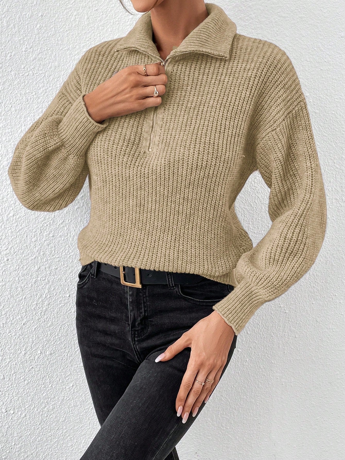 Person wearing a brown knitted sweater and black pants against a white background