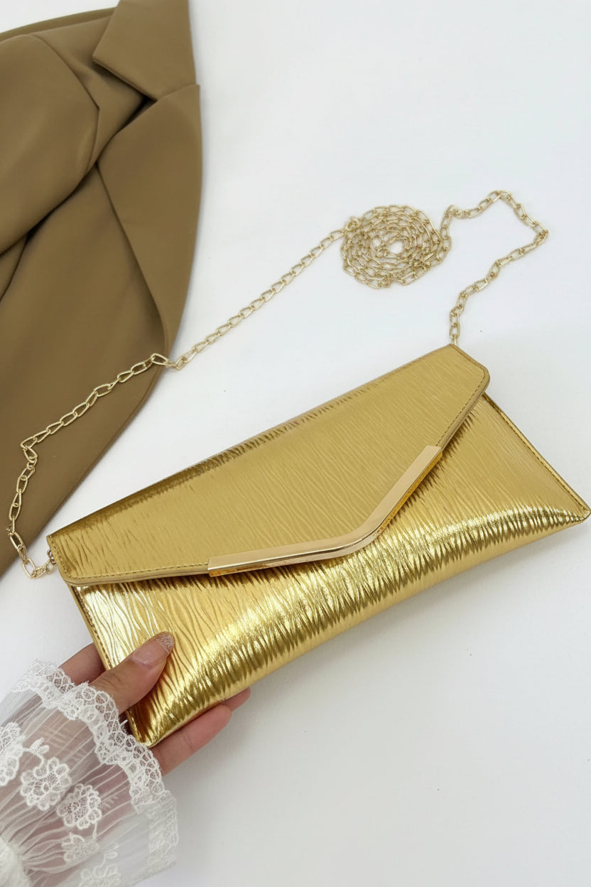 Gold clutch with chain strap held by a hand on a white background