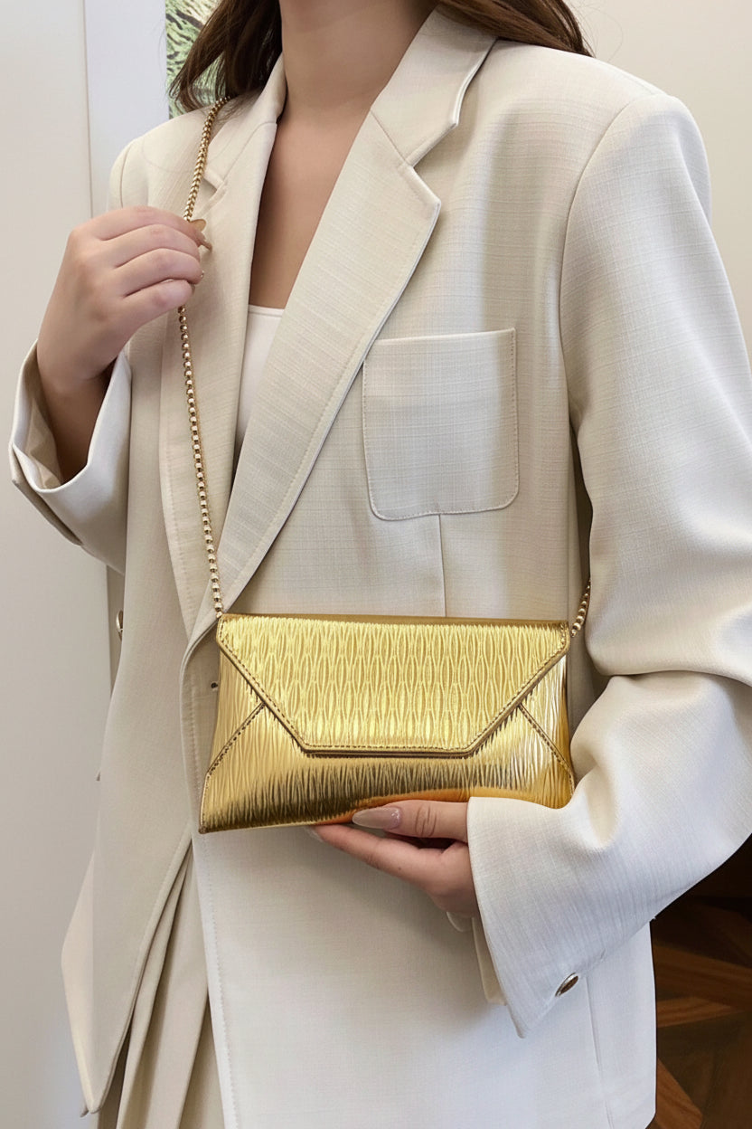 Person holding a gold clutch bag wearing a white blazer indoors.
