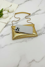 Gold clutch with chain strap holding a phone on a white surface with white tulips.
