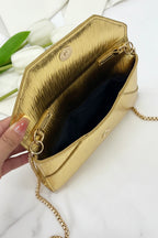 Gold clutch bag held by a hand with white tulips in the background