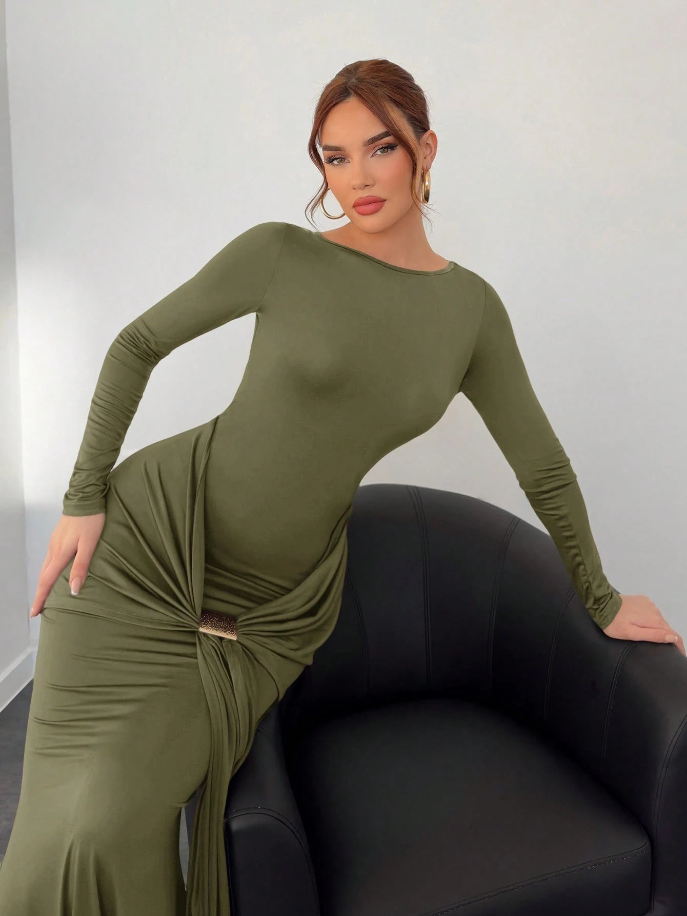 Woman wearing a green dress sitting on a black chair against a white wall