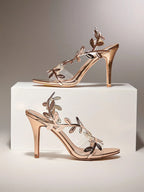 Rose gold high-heeled sandals with floral designs on a white platform against a gray background