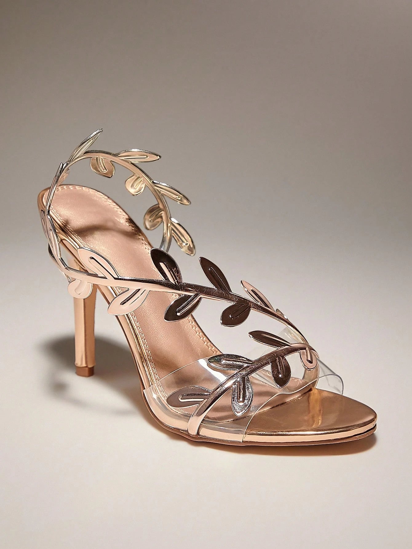 Rose gold high-heeled sandal with leaf-like straps on a neutral background