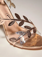 Rose gold sandal with leaf designs on a light background