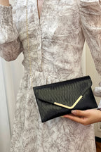 Person holding a black clutch with gold accent against a neutral background