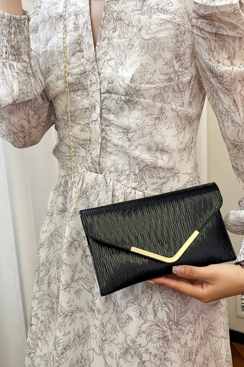 Person holding a black clutch with gold accent against a neutral background