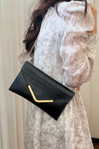 Person holding a black clutch with a gold handle against a neutral background