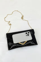 Black clutch with gold chain strap holding a phone on a white surface