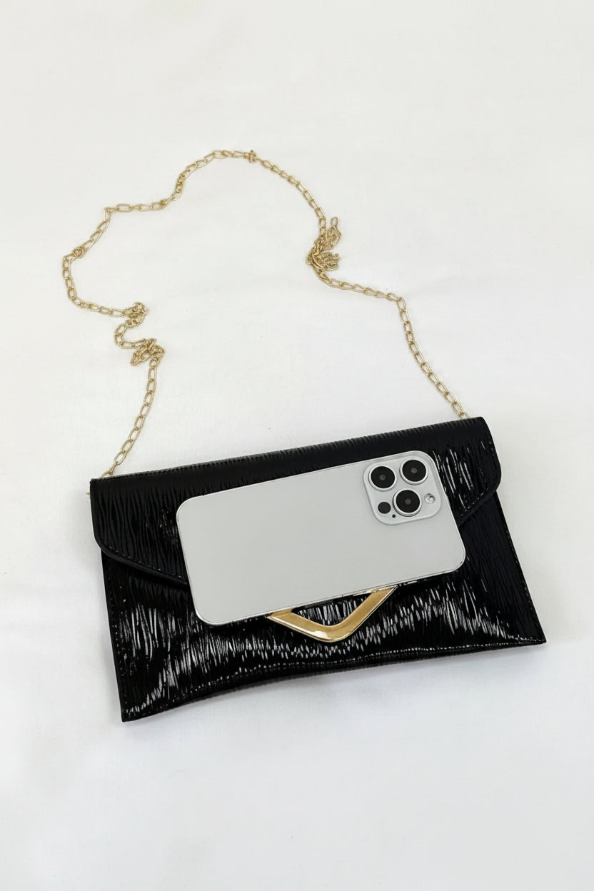 Black clutch with gold chain strap holding a phone on a white surface