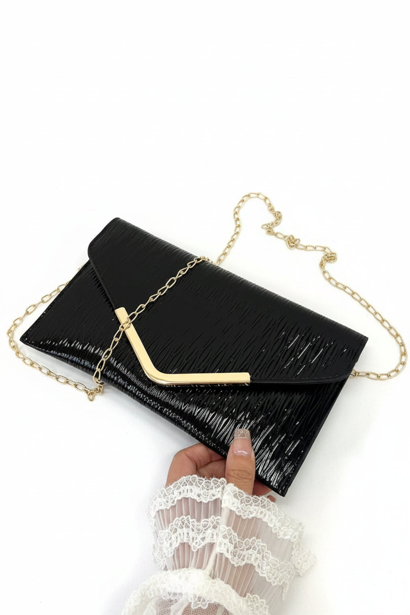 Black clutch with gold chain held by a hand on a white background