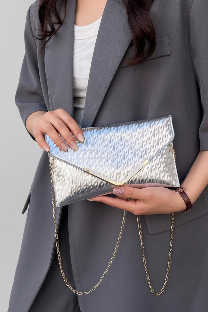 Person holding a silver clutch with a gold chain strap against a neutral background