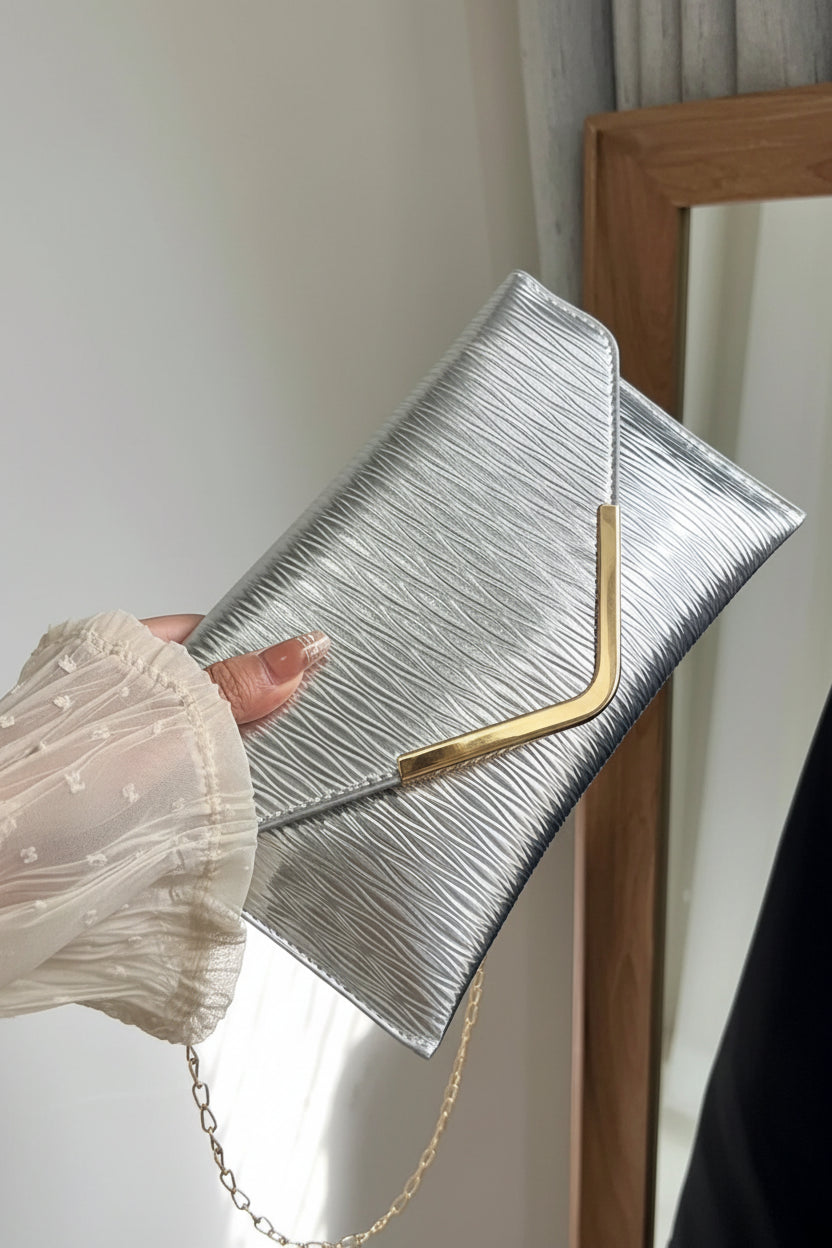 Silver clutch with gold handle held by a hand against a neutral background